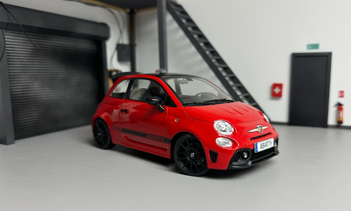 Abarth 595 rouge à bandes noires miniature dans un garage